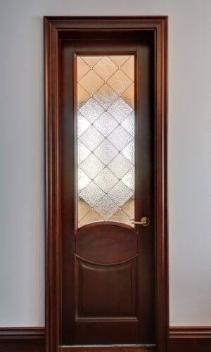 Savannah door glass insert: frosted with a diamond pattern, set in a closed wooden door; brass handle on right.