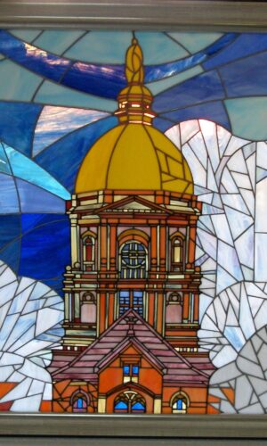 Notre Dame Stained Glass Window with domed building, blue-white backdrop, and “ND” logo in the top left.