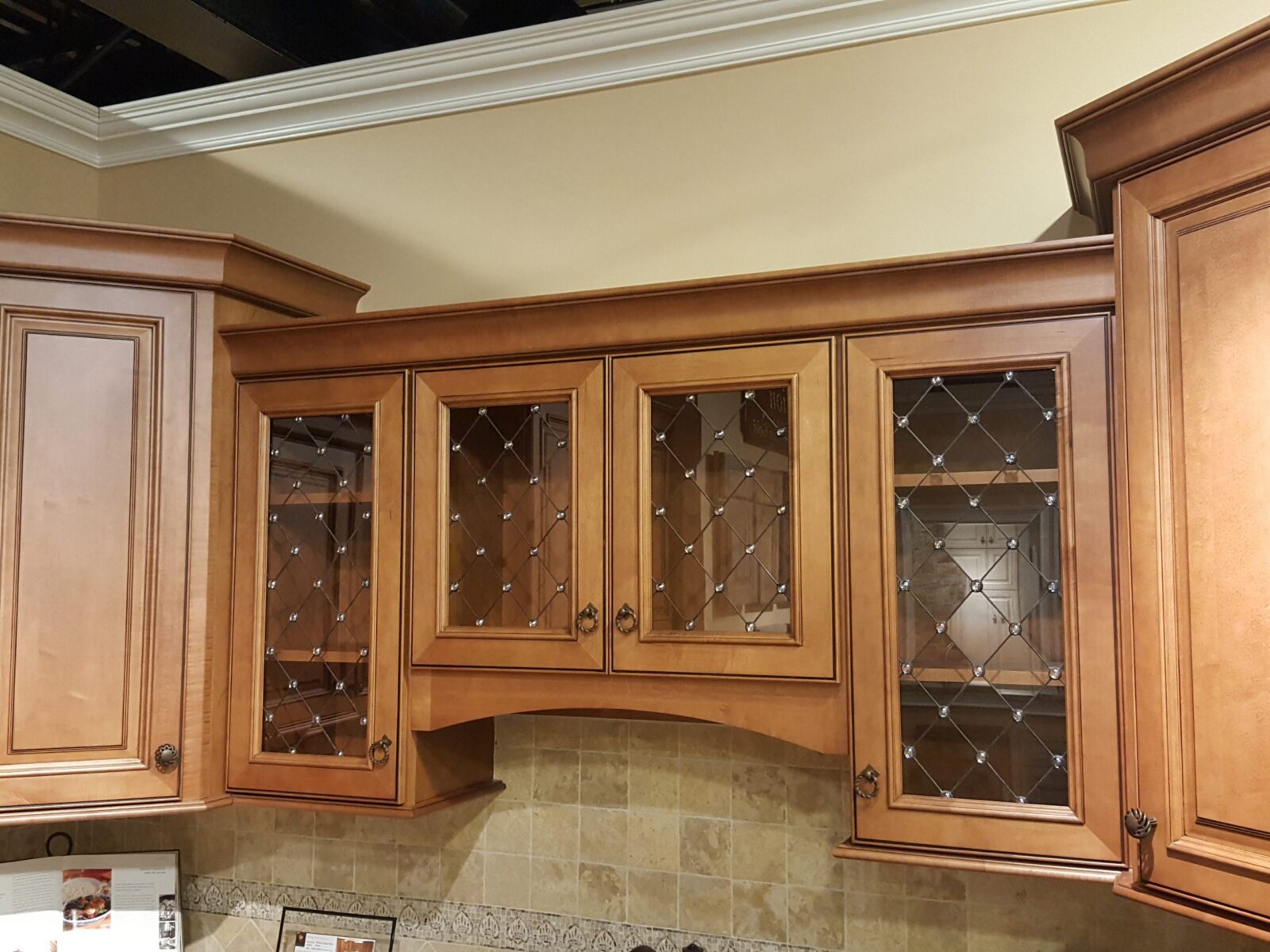 Savannah wood cabinets with diamond-grid art glass doors, installed above a tiled kitchen backsplash.