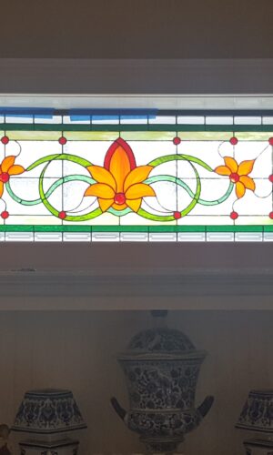 Custom Design Stained Glass Window with orange flower motif displayed above a shelf with decor and a small bottle.