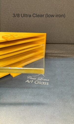 A 3/8″ Thick Ultra Clear Glass Shelf sits on black near a yellow stand, showcasing its tempered, polished clarity.