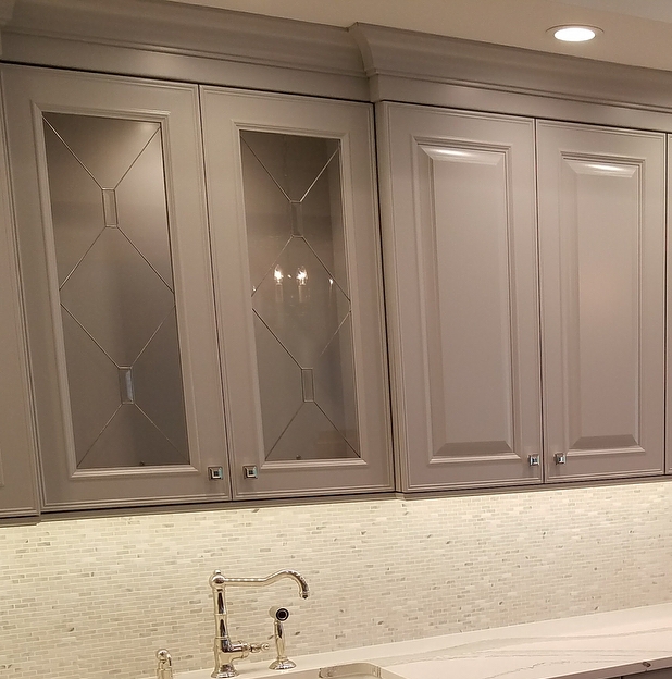Astoria gray cabinets with glass doors, tile backsplash, modern faucet, and a light countertop.