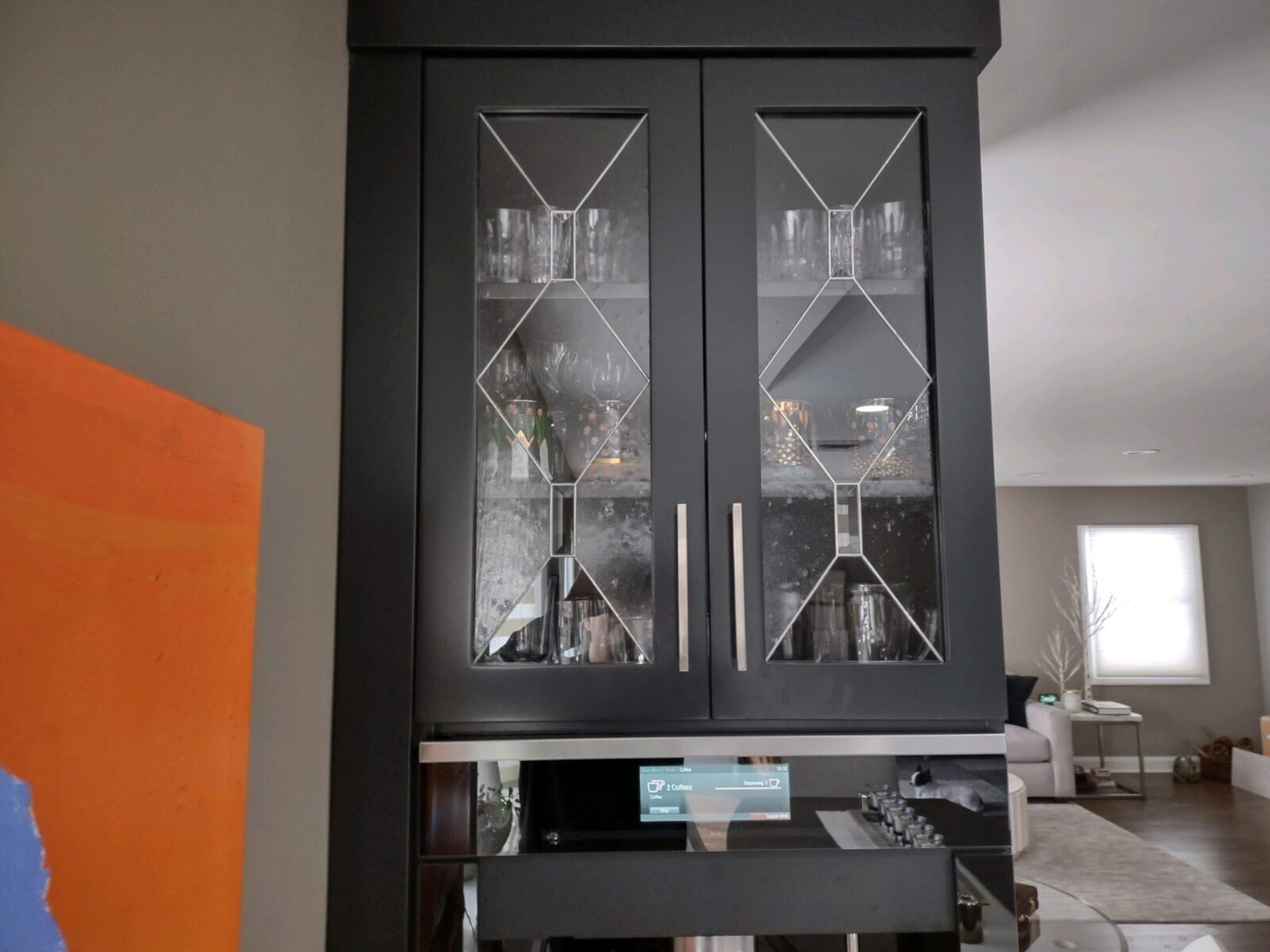 Astoria cabinet with a decorative glass panel displays glassware, accenting a modern space with neutral walls.