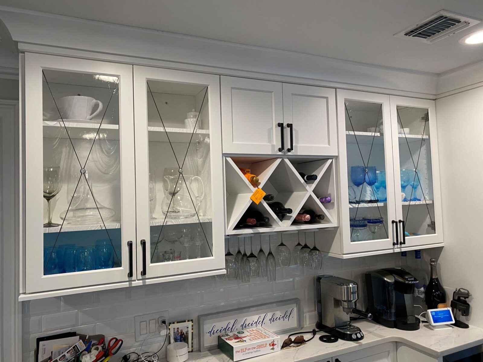 Chester white cabinets with glass doors showcase glassware; shelves store cups, wine, and a coffee maker below.