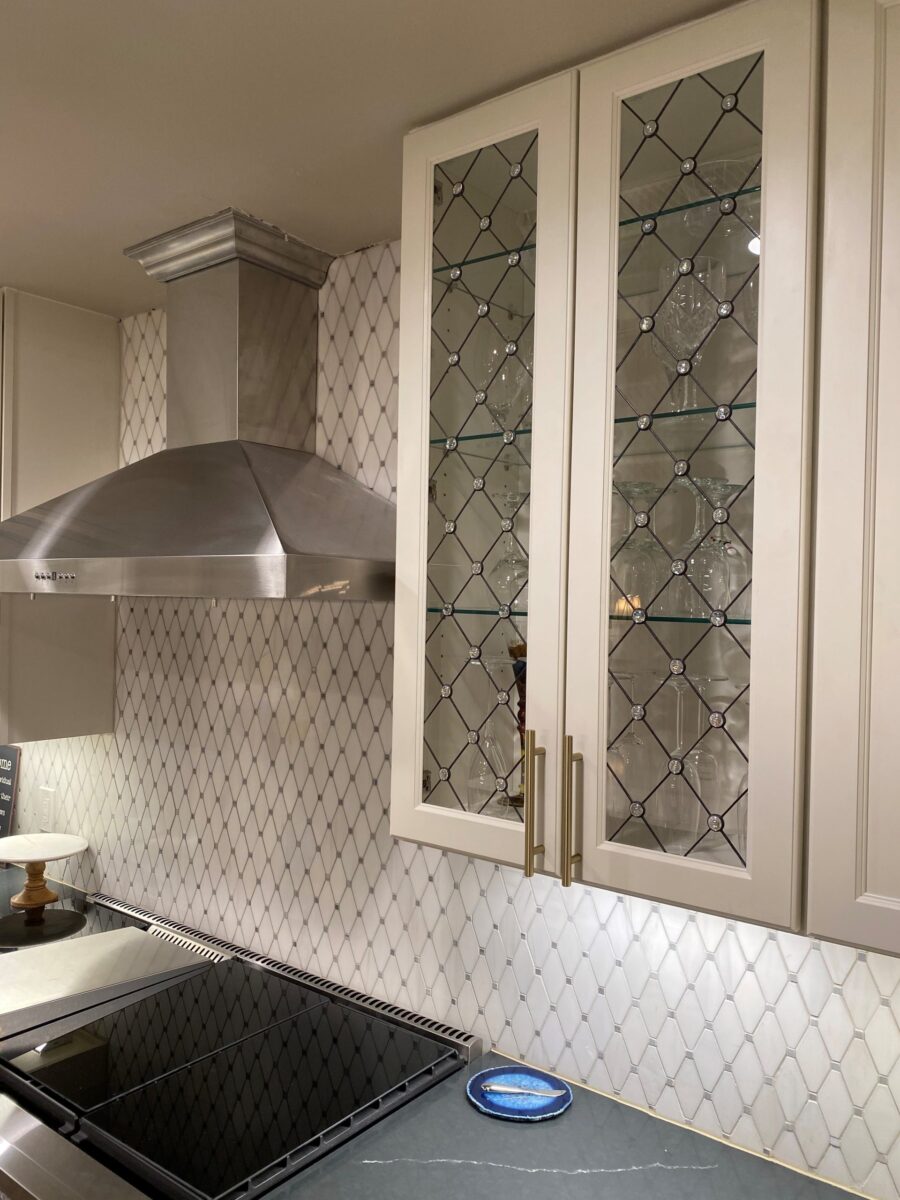 Savannah range hood & cabinets with art glass insert, plus geometric tile backsplash in the kitchen.