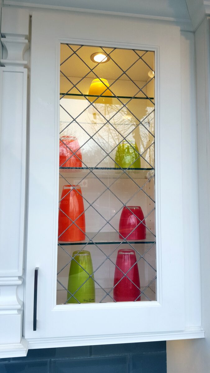 Apollo cabinet with glass front and art glass insert, displaying four colorful vases in red, green, and yellow.