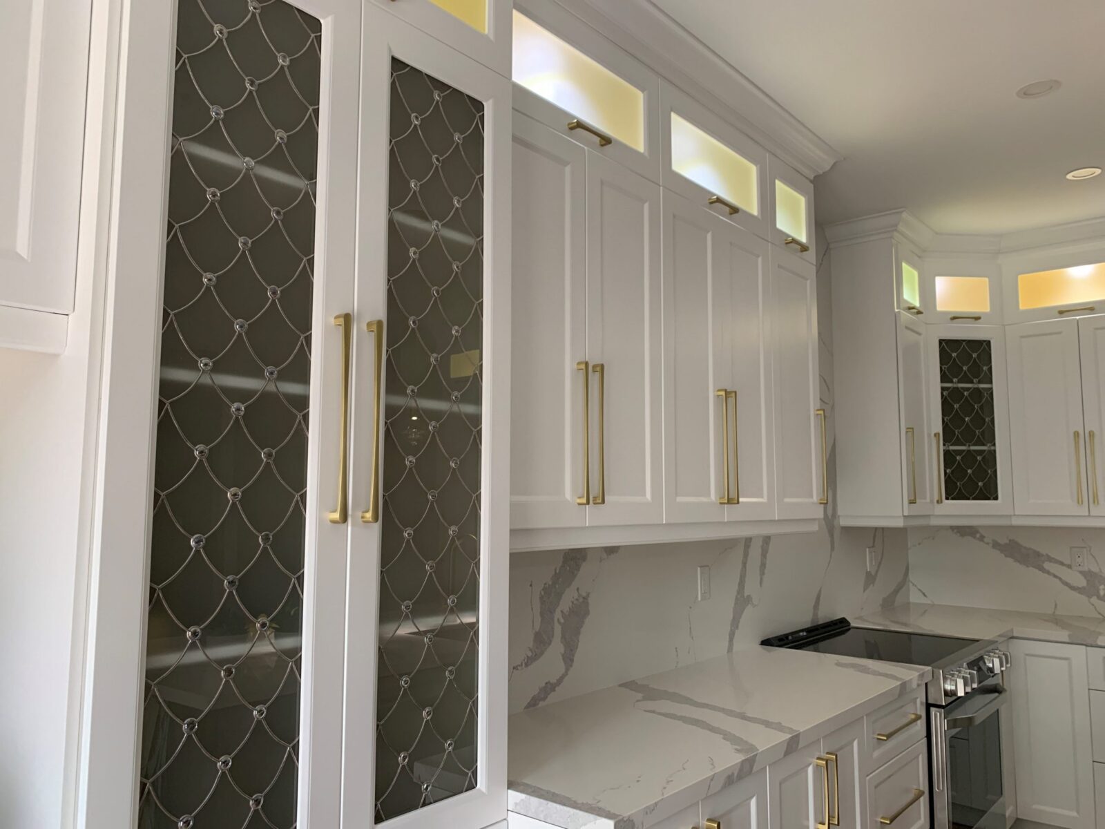 Modern Venezzia kitchen: white cabinets, diamond-patterned glass doors, gold handles, and marble countertops.
