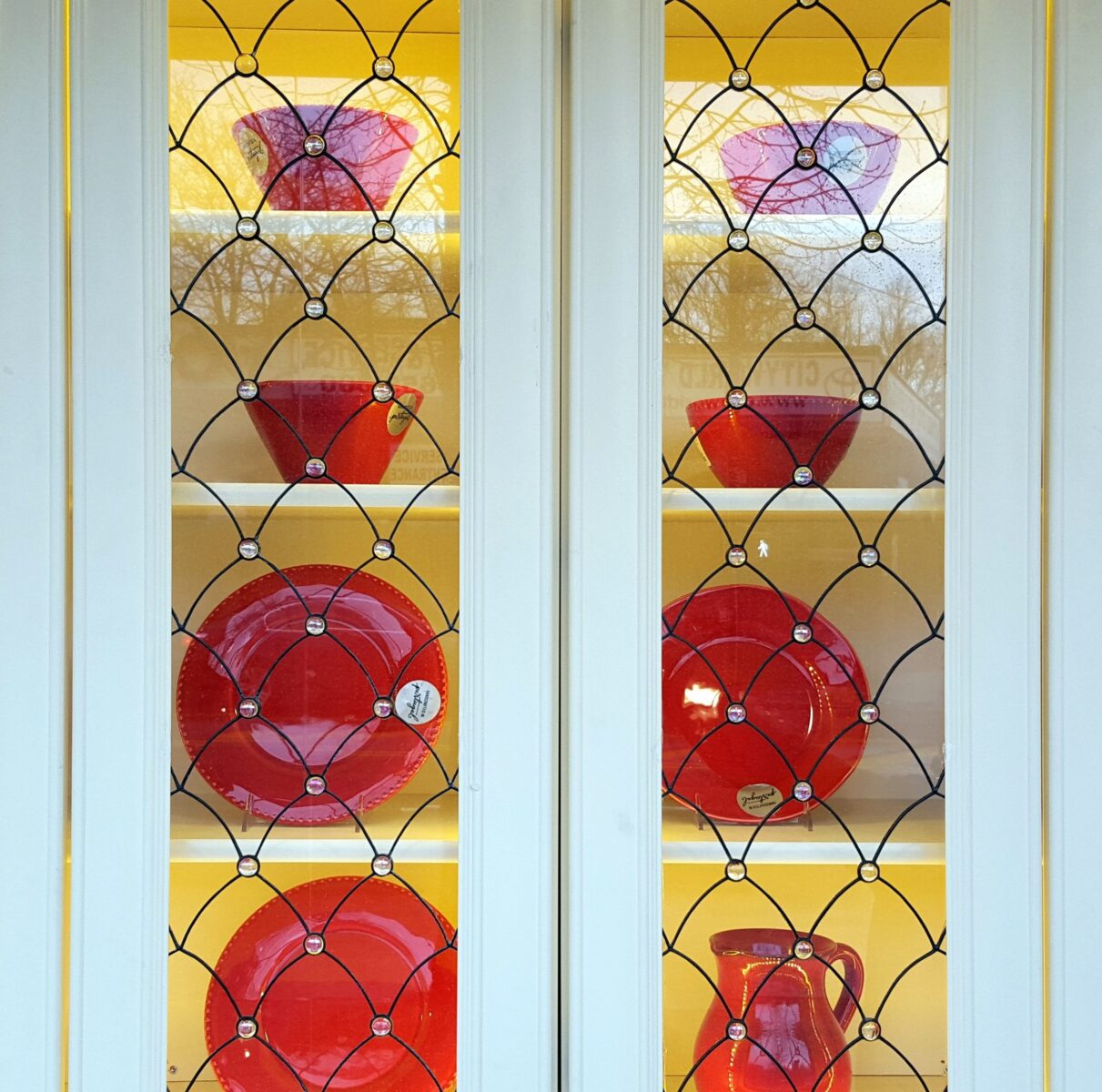 Venezzia cabinet with art glass doors and shelves showcasing red dishes through unique patterned glass design.
