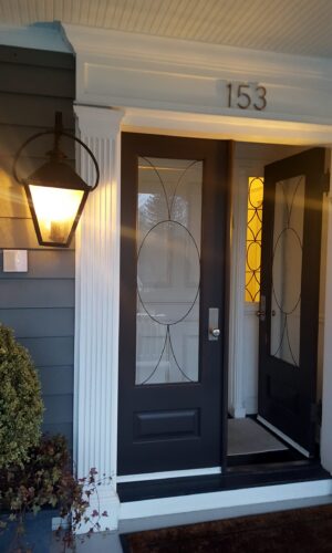 Custom Exterior Door with Custom Glass Insert; house number 153 above, porch light on, door is open.
