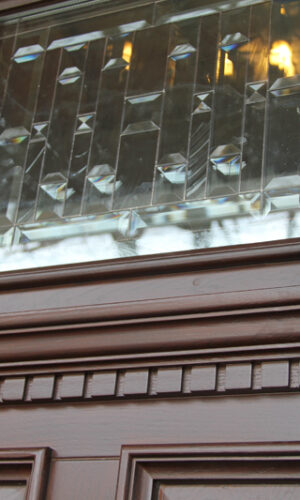 Close-up of a brown wooden door featuring a Beveled Door Glass Insert and carved trim details.