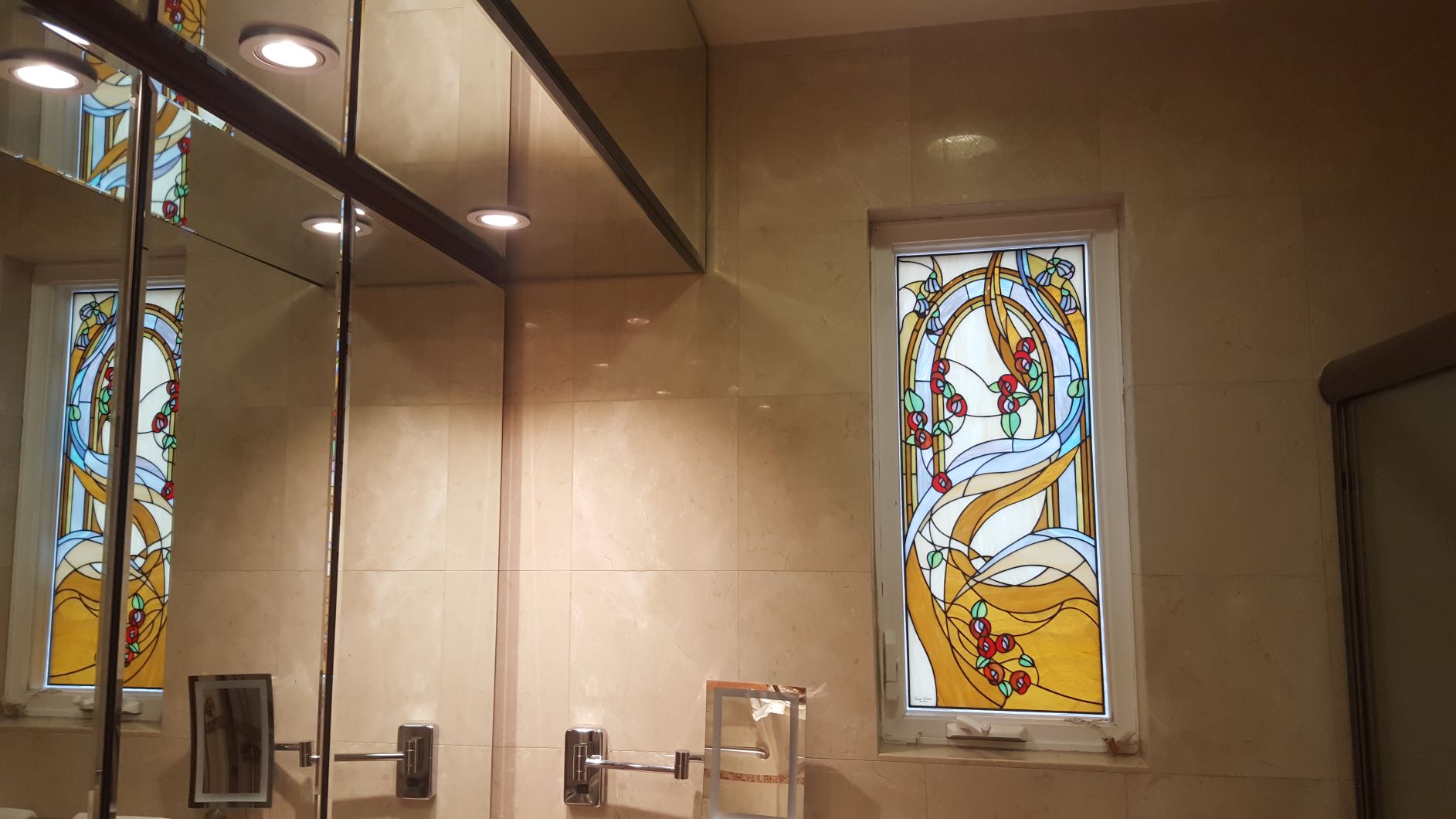 Bathroom with beige tiled walls, a mirror, and a window featuring the Abstract Tree stained glass art.