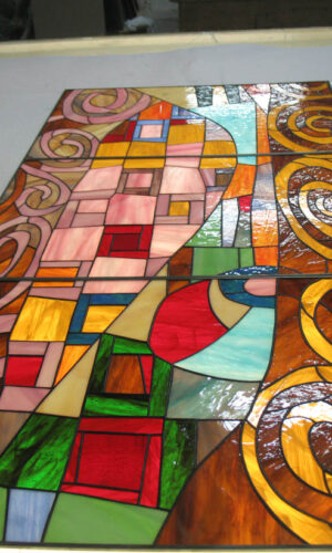 Abstract Art Colorful Stained Glass panel with geometric and swirl patterns on a light gray surface.