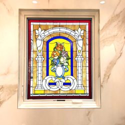 Stained glass window with a floral and arch design set in a beige marble wall under recessed ceiling lights.
