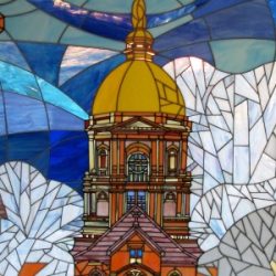 Stained glass artwork depicting a golden-domed building with blue and white geometric shapes in the background.
