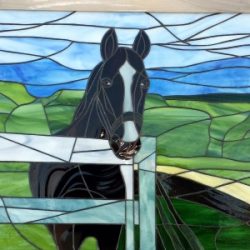 Stained glass artwork depicting a black horse with a white stripe standing by a fence in a green field.