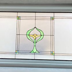 Rectangular stained glass window with geometric borders and a central green, yellow, and blue floral design.