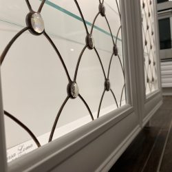 Close-up of a decorative glass cabinet door with diamond-shaped metal grid and round glass accents, next to a kitchen.