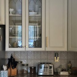 White kitchen cabinets above a counter with a knife block, toaster, tissue box, canisters, and small kitchen items.