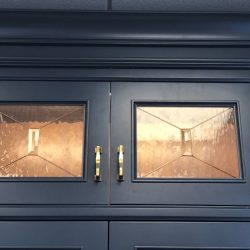 Dark blue cabinets with two brass-handled doors, each featuring a glass panel with a metallic geometric design inside.