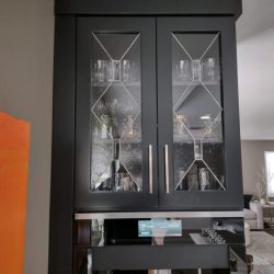 Black cabinet with glass doors displaying glassware, set against a neutral wall in a modern living space.
