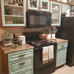 A kitchen with mint green cabinets, a black stove and microwave, a coffee maker, and various utensils on the counter.