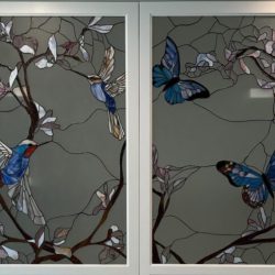 Stained glass panels depicting blue birds and butterflies among branches with leaves on a muted background.