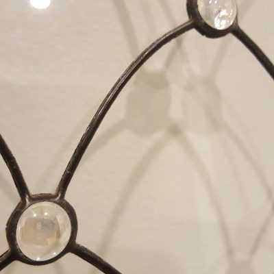 Close-up of black metal lattice with clear glass gems at intersections, casting shadows on a light-colored surface.
