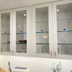 White kitchen cabinets with glass doors display dishes and glasses; counter holds a toaster, plant, and knife block.
