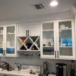 White kitchen cabinets with glass doors display glassware; countertop holds appliances, a bottle, and a box.