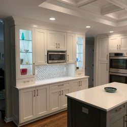 Modern kitchen with white cabinets, a built-in microwave, double ovens, glass shelves, and a central island.