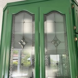 Green cabinet doors with textured glass panels and diamond-shaped leaded designs, reflecting a window view.
