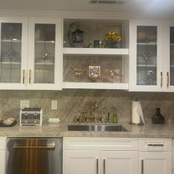 Modern kitchen with white cabinets, a sink, toaster, stove, decorative items, and glass-front upper cabinet doors.