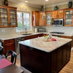 Modern kitchen with wood cabinets, granite countertops, island, stainless appliances, and dining table with placemats.
