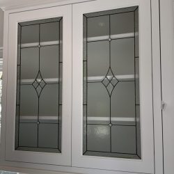 White kitchen cabinet with two glass doors featuring geometric stained glass designs and a small cabinet knob.