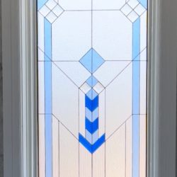 Rectangular stained glass window with geometric blue and white patterns set in a white frame.