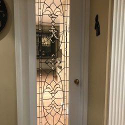White door with decorative glass panel featuring geometric and floral designs, leading to a well-lit room.