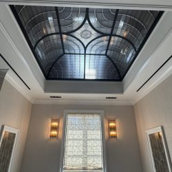 Room with a decorative glass skylight ceiling, a window with a shade, and two wall sconces on either side of the window.