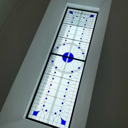 Rectangular stained glass skylight with geometric patterns and blue accents set in a white ceiling.
