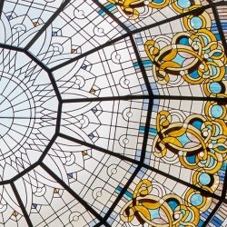 Circular stained glass ceiling with geometric lines and ornate gold, blue, and white decorative patterns.