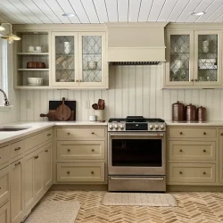 Beige kitchen with glass cabinets, stainless steel stove, farmhouse sink, and herringbone wood floor.