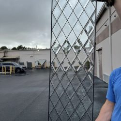 Person holding a rectangular glass panel with a diamond pattern, outdoors near a building on a cloudy day.