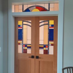 Double wooden doors with colorful geometric stained glass panels and matching transom window above.