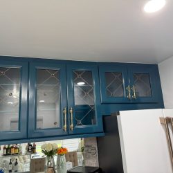 Blue kitchen cabinets with glass panel doors and gold handles above a white refrigerator and dining area.