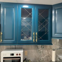 Blue kitchen cabinets with gold handles, a glass front, and a white toaster oven on a marble countertop below.