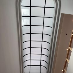 Oval skylight with grid pattern in a white ceiling, adjacent to a wall with wooden shelves and recessed lighting.
