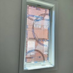 Rectangular window with decorative frosted glass featuring intersecting curved and straight lines; sunlight enters the room.