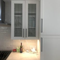 White kitchen cabinets with glass doors above a counter, under-cabinet lighting, and kitchen items on the countertop.