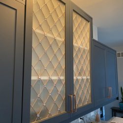 Blue kitchen cabinets with glass doors featuring a diamond lattice pattern and copper handles above a counter.