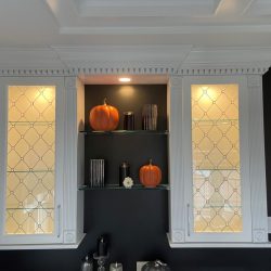 Two orange pumpkins and decorative items are displayed on glass shelves between two illuminated cabinets.