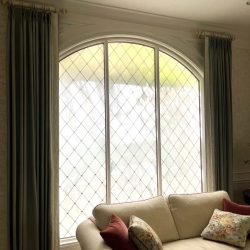 A cream sofa with patterned pillows sits in front of a large arched window with diamond-patterned frosted glass.